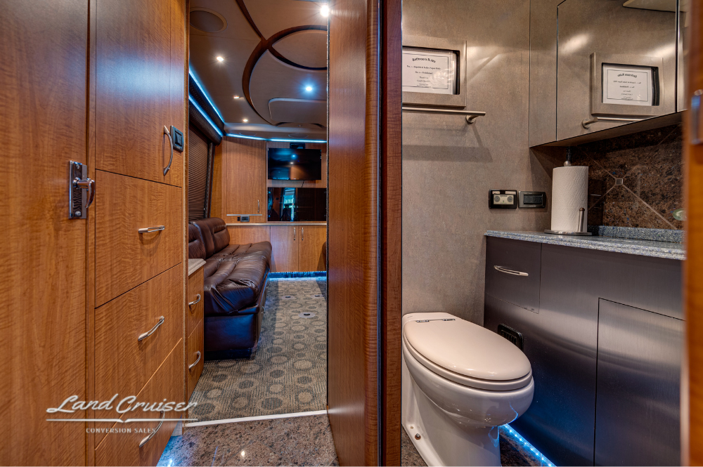 Mid-bathroom view with toilet, vanity, and access to rear lounge through hallway.