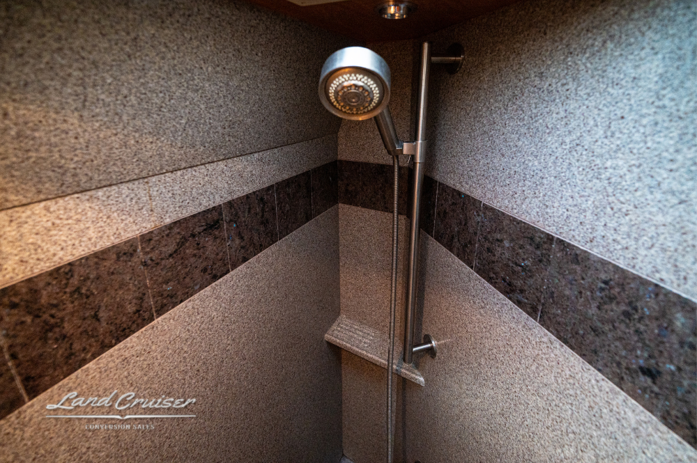 Coach shower with stainless rain head and stone-accented tile walls.