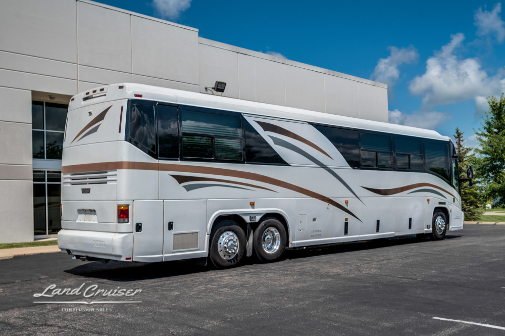 Rear driver-side view of white MCI motorhome with brown and gold accent stripes