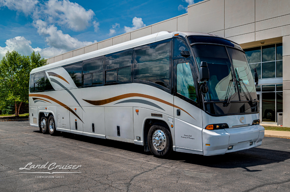 Front side view of 1999 MCI 102EL3 motorhome “Sunset” parked in lot under blue sky