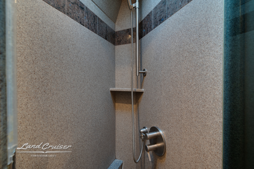 Walk-in RV shower with adjustable handheld sprayer and granite-style walls.