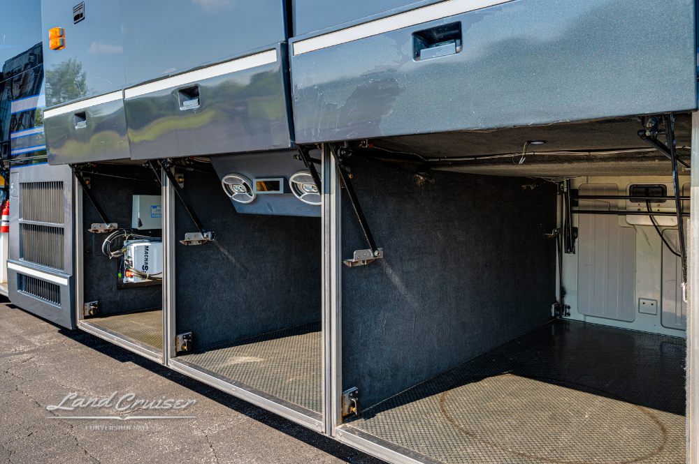 Open cargo bays on the curbside of the entertainer coach, showing storage space with AV wiring access.